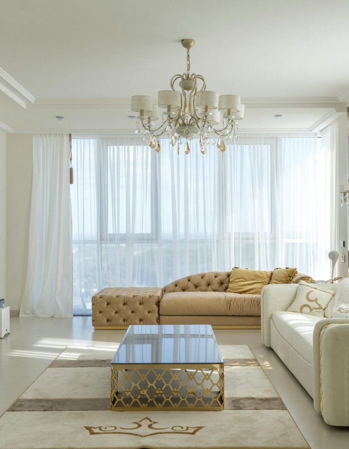 Interior of spacious room with huge windows behind curtains and comfortable furniture against TV set